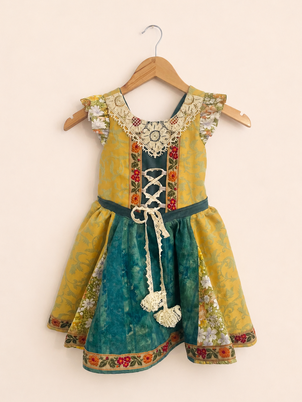 Green and gold witch children's dress with floral patterns on a beige background